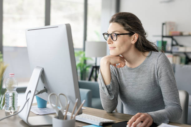 Professional woman sitting at desk and connecting with her computer, she is working from home